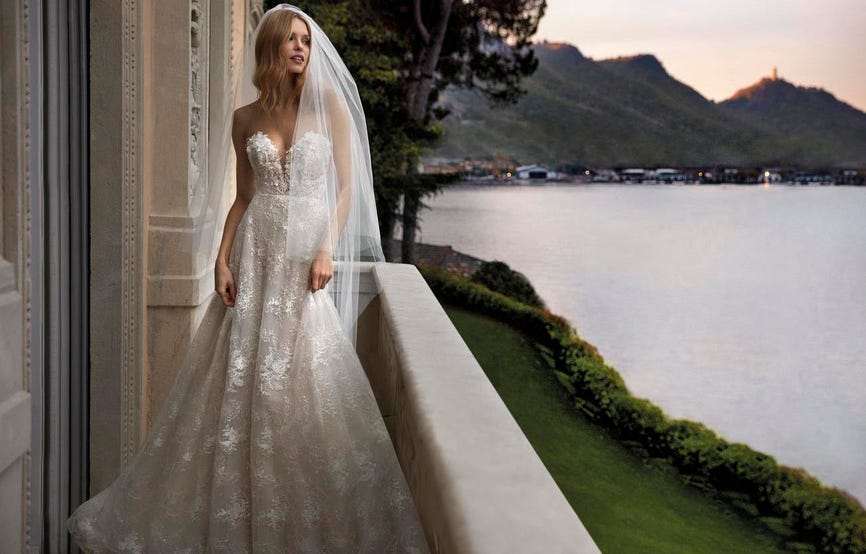 Sposa che si affaccia da un terrazzo e osserva il panorama indossando un vestito in pizzo e un lungo velo in tulle.