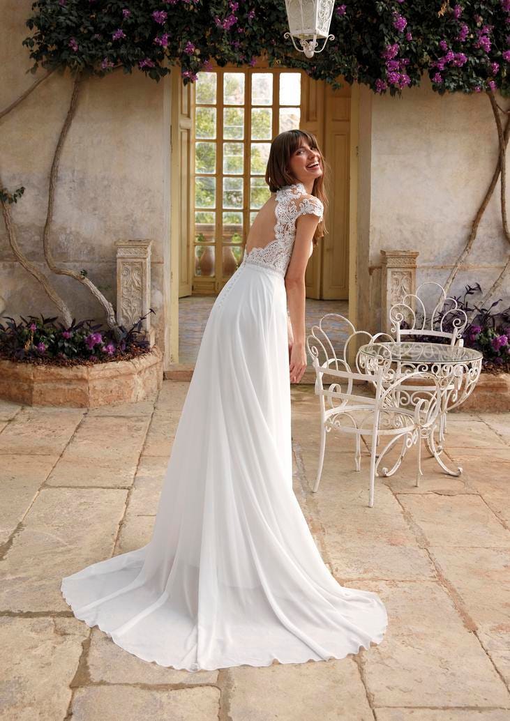 Mariée souriante se tenant au centre d’un petit patio fleuri et élégant destiné à un mariage intime.