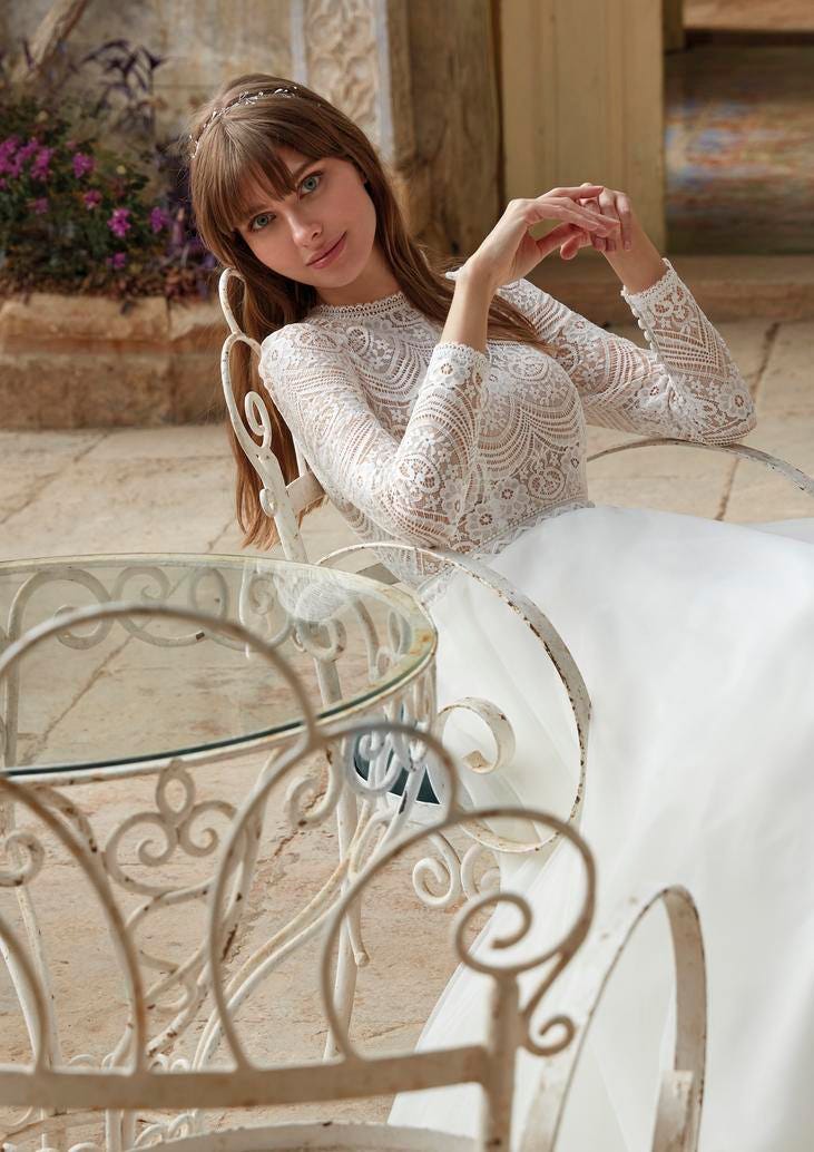Sposa seduta su una sedia che indossa un abito moderno con corpetto con motivi geometrici e gonna in tulle.