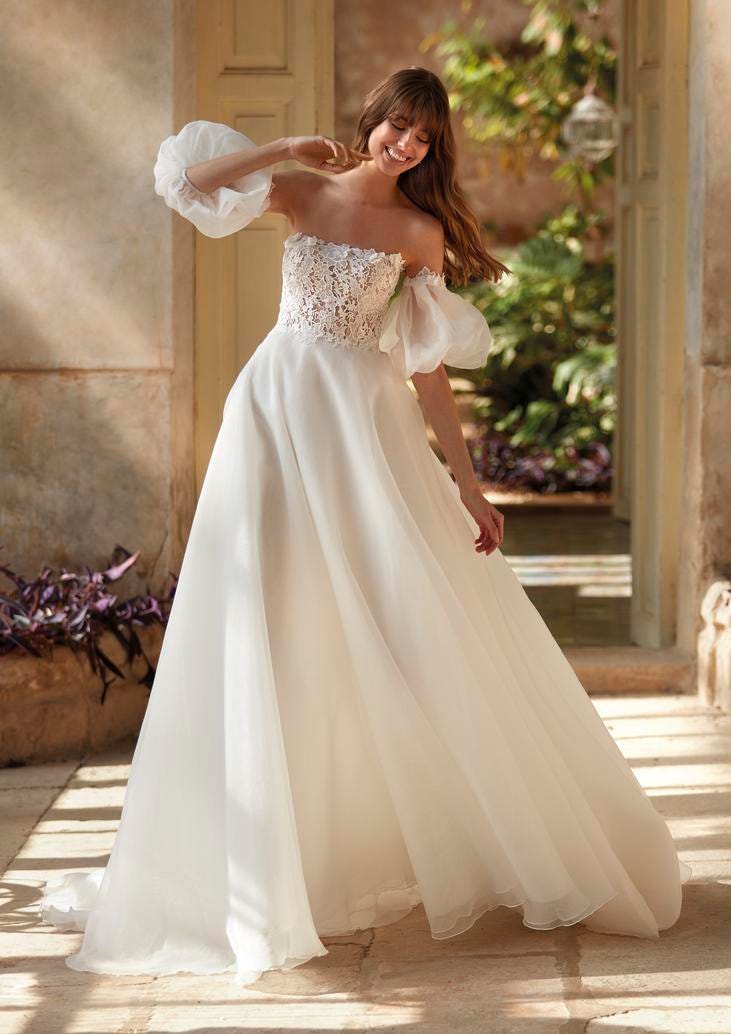 Donna ripresa in movimento con abito da sposa principessa in organza con maniche staccabili a sbuffo e corpetto ricamato.